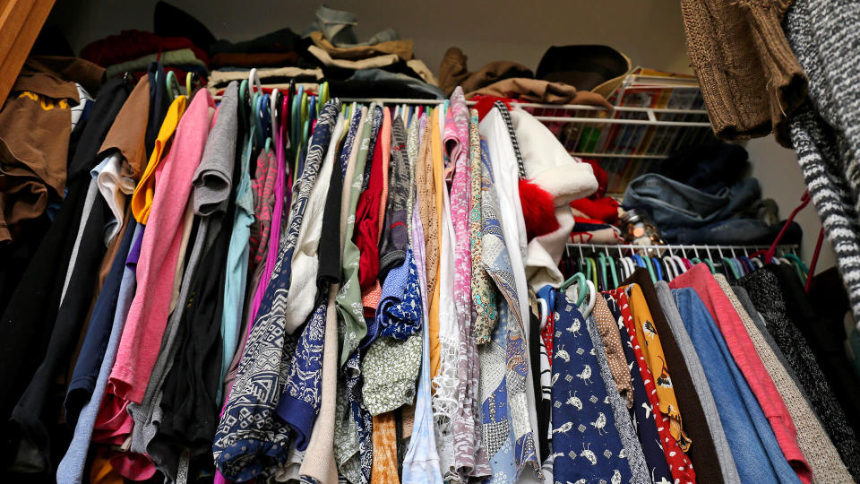 A messy young women's closet is fill with many outfits of colorful clothing, shirts, and dresses.