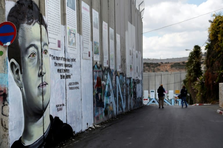 Two men walk past a new piece of graffiti depicting Chief Executive Officer and founder of Facebook Inc Mark Zuckerberg on the controversial Israeli separation barrier separating the West Bank town of Bethlehem from Jerusalem on October 15, 2017