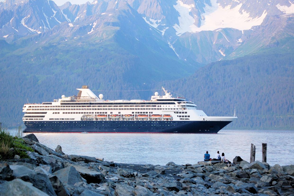 Cruise ship leaving Seward Harbor, Seward, Alaska at sunset, rocks in the foreground with people watching and mountains in the background