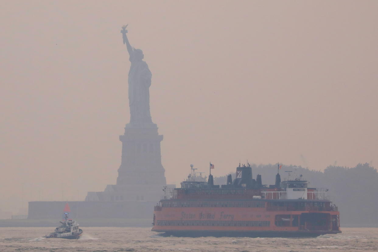 Boats in front of the Statue of Liberty, which is seen through a cover of wildfire smoke