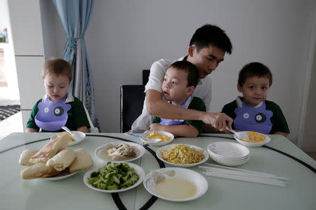 An Hui's partner Ye Jianbin helps their triplets (L-R) An Zhiya, An Zhizhong and An Zhifei eat breakfast at home in Shenzhen, Guangdong province, China September 18, 2018. The triplets were conceived with the help of a German egg donor. REUTERS/Jason Lee