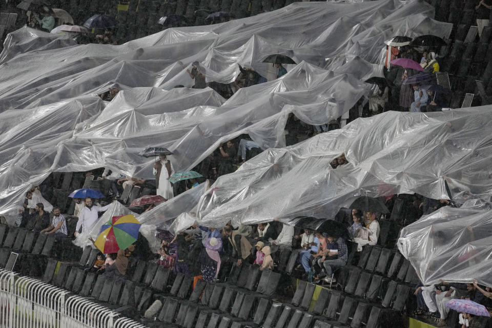Fans cover themselves in plastic sheets as rain stop the play of first T20 cricket match between Pakistan and New Zealand, in Rawalpindi, Pakistan, Thursday, April 18, 2024. (AP Photo/Anjum Naveed)