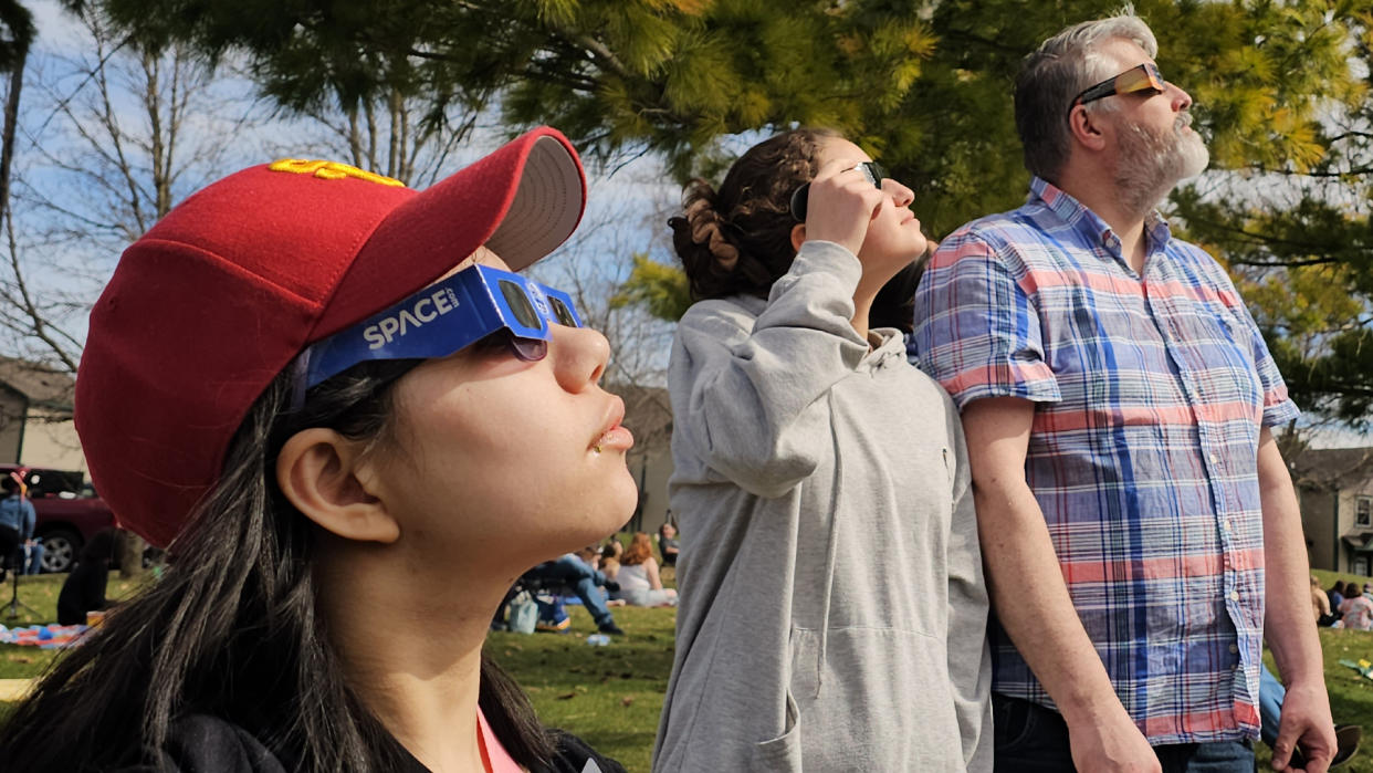  Two girls and a man observe the total solar eclipse of April 8, 2024 with eclipse glasses. 