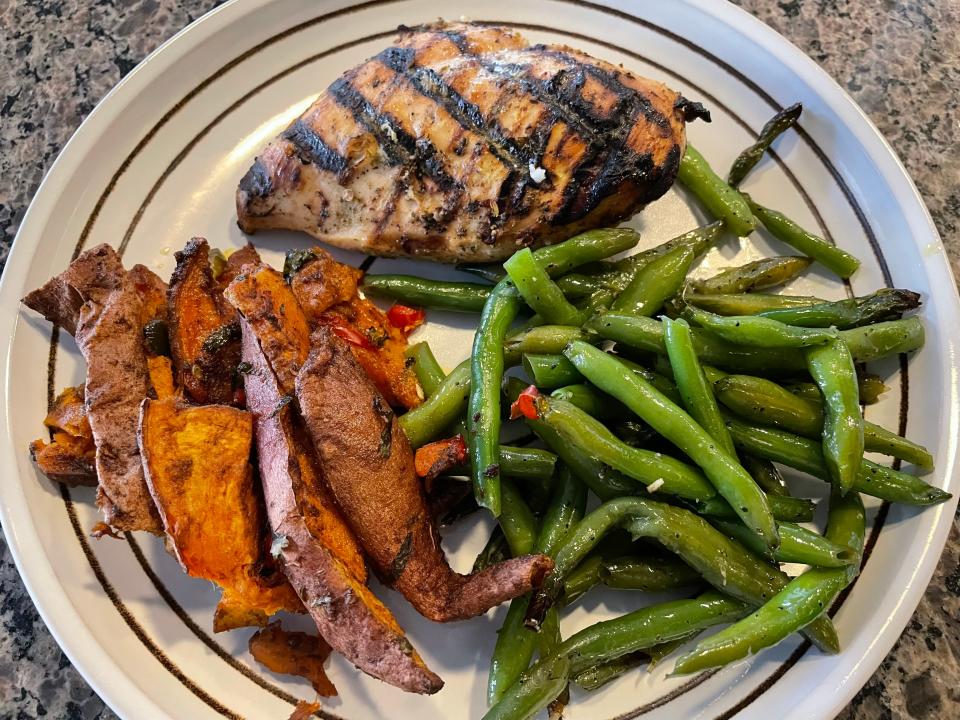 A chicken breast with grill marks on it, green beans, and sweet potatoes on a white plate