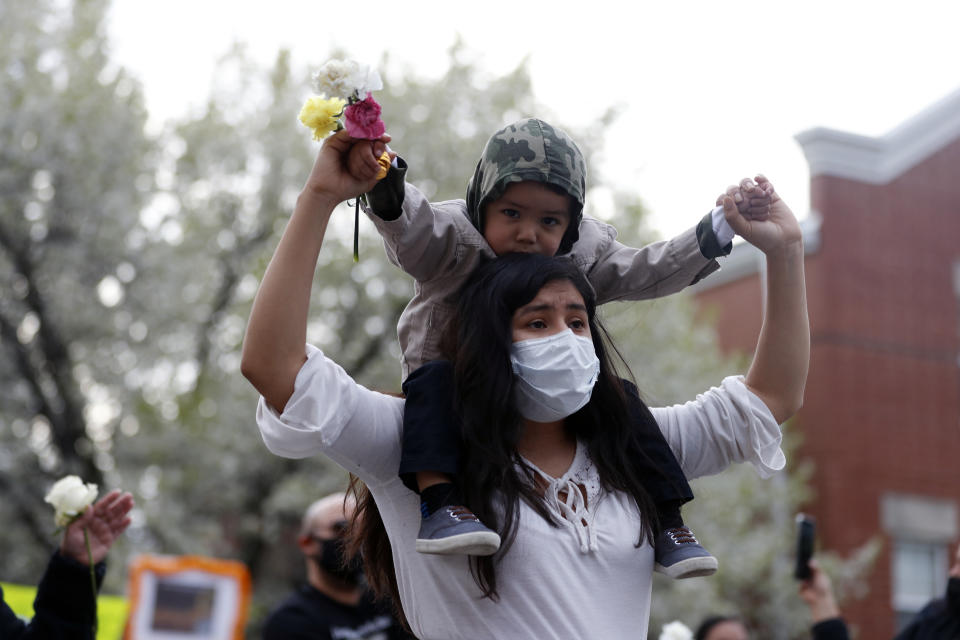 A woman carrying a kid raises her hand as they attend a peace walk honoring the life of police shooting victim 13-year-old Adam Toledo, Sunday, April 18, 2021, in Chicago's Little Village neighborhood. (AP Photo/Shafkat Anowar)