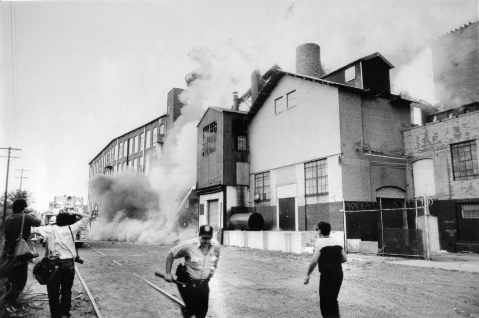 Emergency crews took cover as the Passaic fire caused a wall of a building to collapse near Ninth Street in Passaic, N.J., on September 2, 1985. Six former textile buildings and 17 multifamily homes are destroyed by fire, forcing the evacuation of 400 people. The blaze which began around 2:30 p.m. destroyed the facilities of more than 50 manufacturers in the complex along the Passaic River.