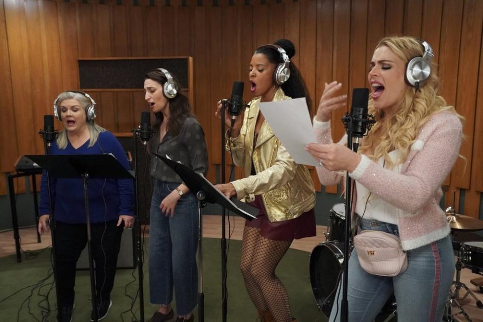 Four women in headphones sing into microphones in a recording studio.