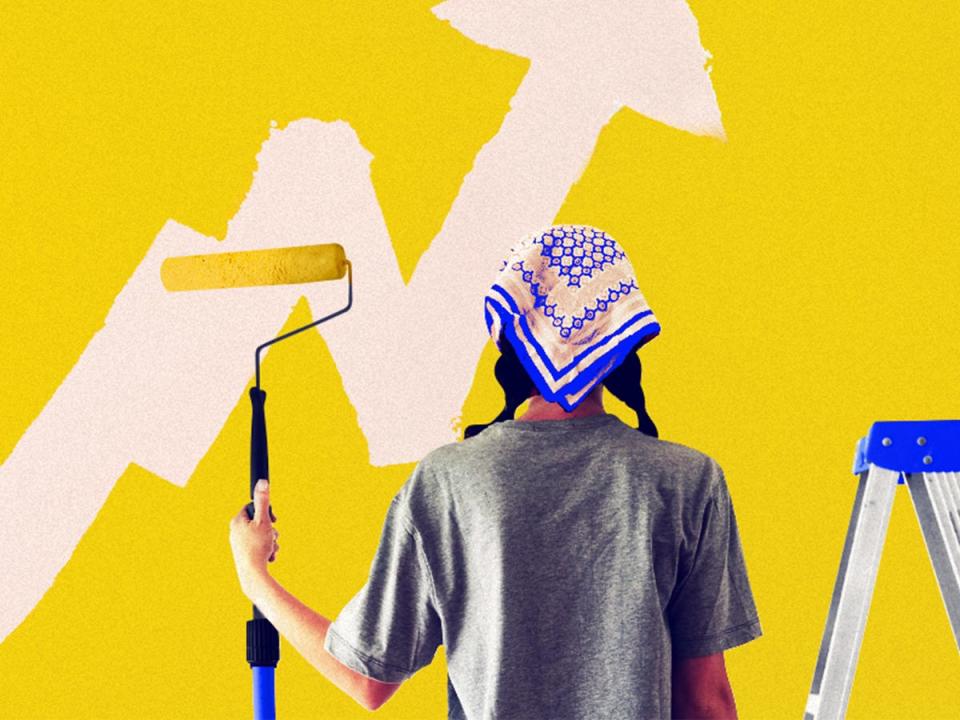 Young millennial woman holding a paint roller, seen from behind, in the process of painting over an upward trending line