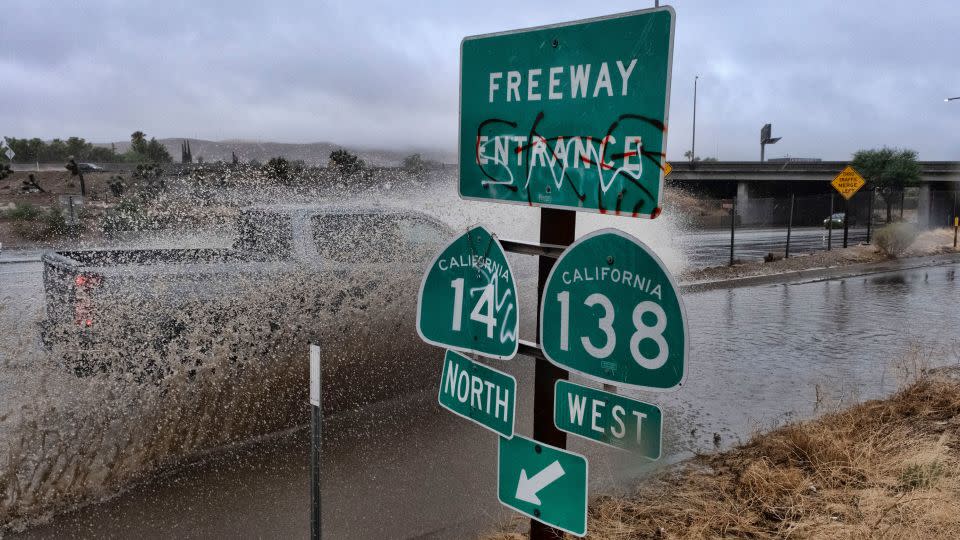 A vehicle engulfed in water drives through a flooded freeway entrance in Palmdale, California.  - Richard Vogel/AP
