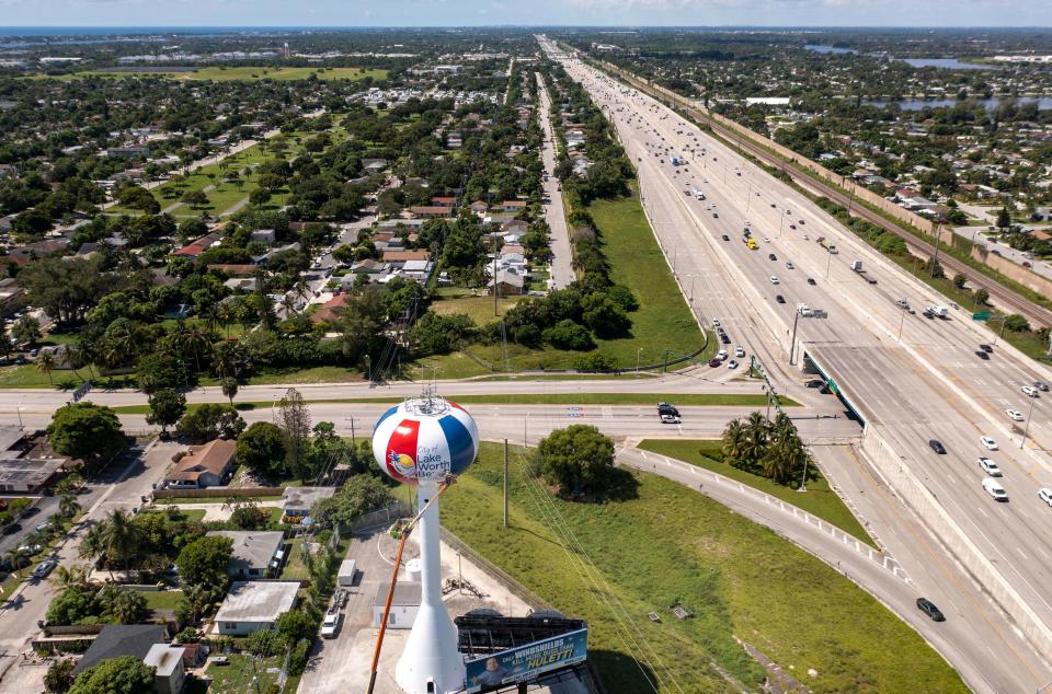 Jimmy Kelly stands on a lift as he paints the water tower next to Interstate 95 in Lake Worth Beach, Florida on August 4, 2023.