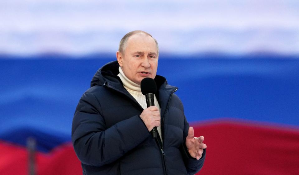 Russian President Vladimir Putin holds a microphone as he gives a speech at a stadium.