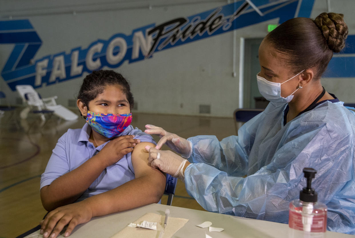 Tracy Jones, a licensed vocational nurse, places a bandage on the arm of Angel Macias, 12, a seventh grader at San Fernando Institute for Applied Media in San Fernando, Calif., after giving the student the first dose of the Pfizer vaccine.