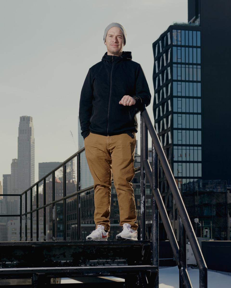 A man in a zip-up jacket and a beanie poses in New York.