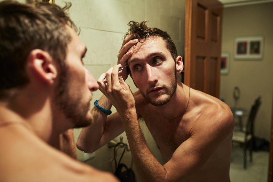 A man plucking his eyebrows in the mirror