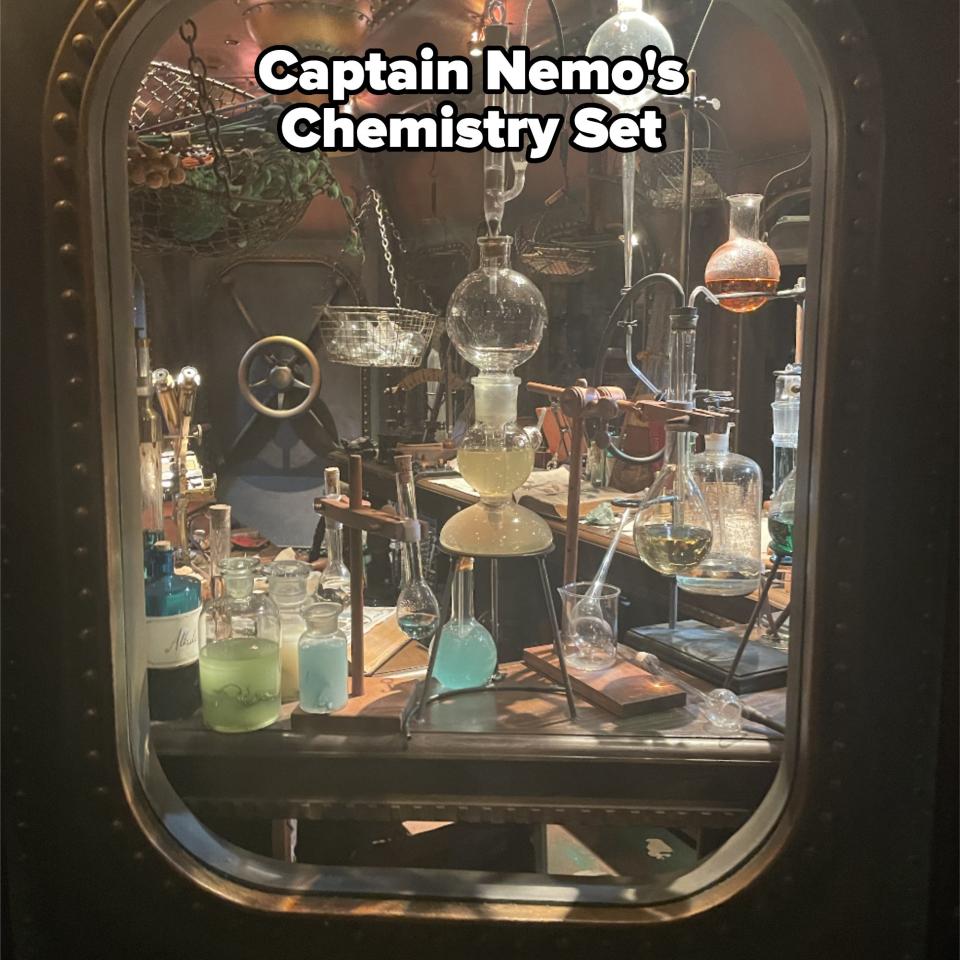 A laboratory with various glass beakers, flasks, and tubes filled with colorful liquids, as seen through a porthole-like window. No people are present