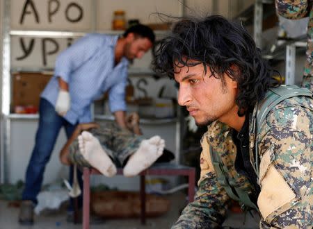 A Syrian Democratic Forces (SDF) fighter sit as medics treat his comrades injured by sniper fired by Islamic State militants in a field hospital in Raqqa, Syria June 28, 2017. REUTERS/Goran Tomasevic