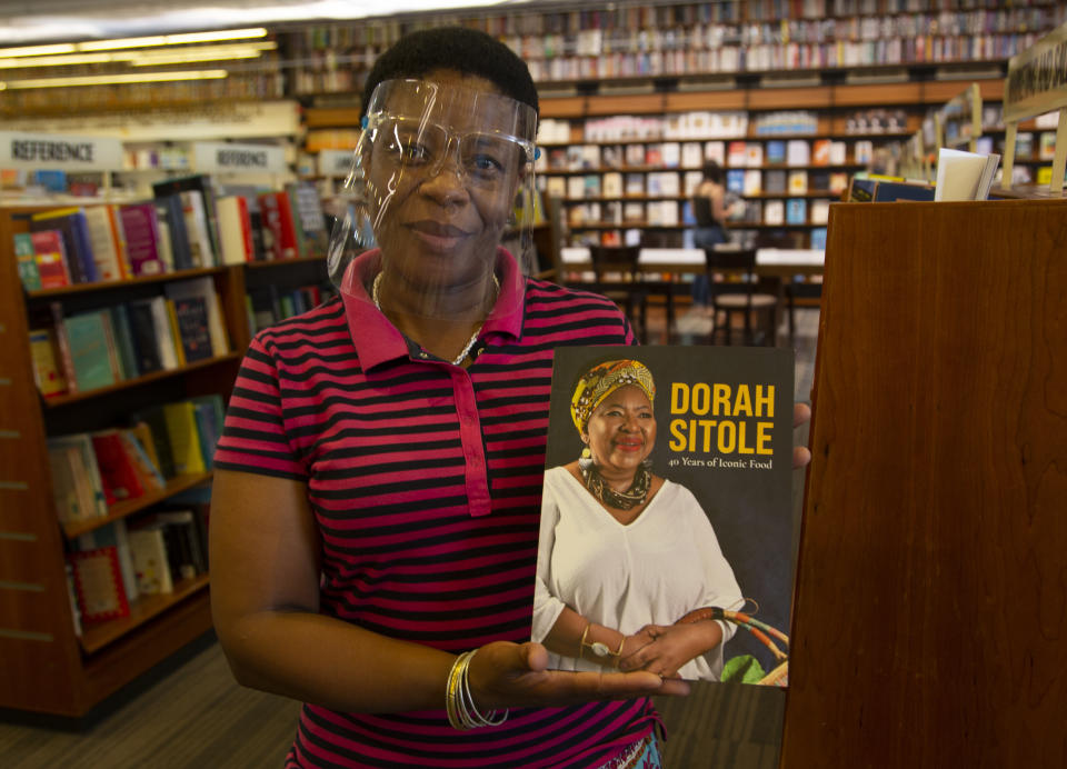 Book store worker, Dikeledi Nhlapo, holds a copy of Dorah Sitole's "40 Years of Iconic Food" cook book in Exclusive Books in Hyde Park Corner, Johannesburg, Tuesday, Jan. 12, 2021. South Africa's pioneer Black food writer Sitole, portrait on cover, who quietly defied apartheid to win respect and a wide readership for African cuisine, died January 2021, of COVID-19. (AP Photo/Denis Farrell)