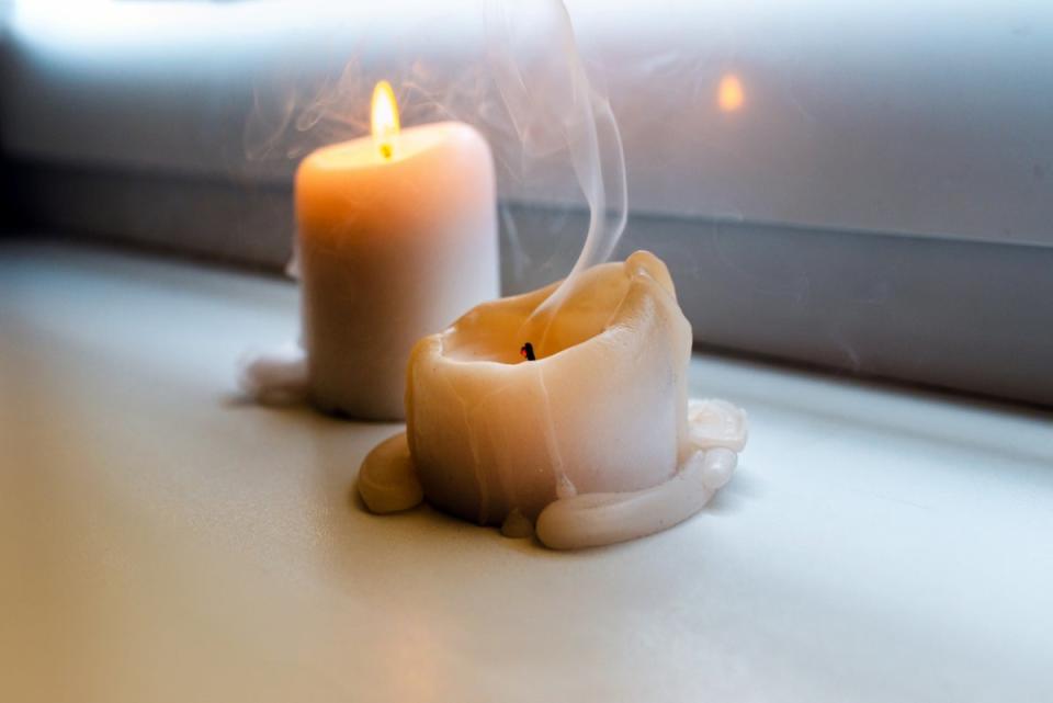 Two candles by windowsill and one blown out.