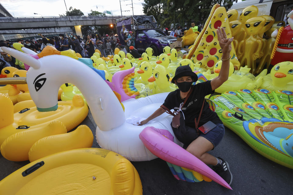 CORRECTS PHOTOGRAPHER'S NAME - A woman flashes a three-finger protest gesture while posing in front of mostly inflatable yellow ducks, which have become good-humored symbols of resistance during anti-government rallies, Friday, Nov. 27, 2020 in Bangkok, Thailand. Pro-democracy demonstrators are continuing their protests calling for the government to step down and reforms to the constitution and the monarchy, despite legal charges being filed against them and the possibility of violence from their opponents or a military crackdown. (AP Photo/Wason Wanichakorn)