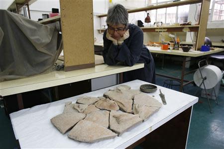 An Israel Antiquities Authority (IAA) employee looks at parts of a broken coffin and other artefacts displayed for the media, at IAA offices in Jerusalem April 9, 2014. REUTERS/Ronen Zvulun