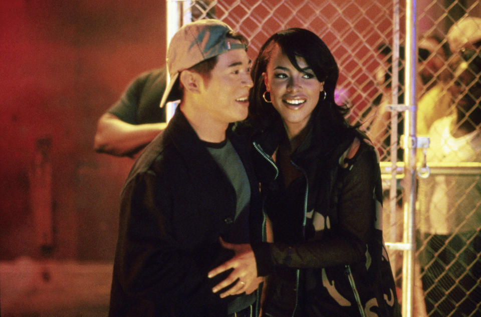 A Black woman and Asian man smile and hug standing in front of a fence