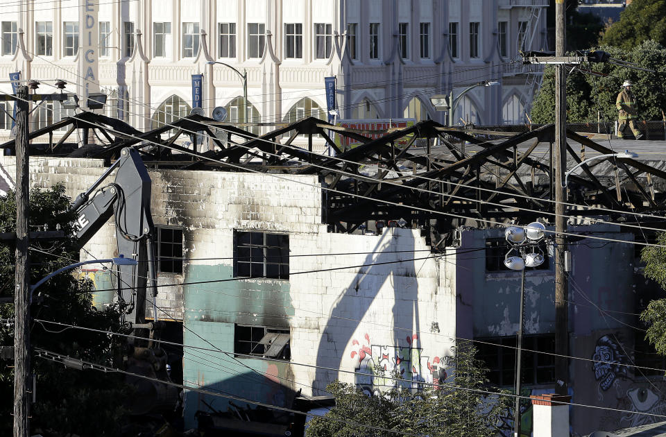 FILE - In this Dec. 6, 2016 file photo, an emergency crew worker, top right, walks on a roof next to the site of a warehouse fire in Oakland, Calif. A judge will hear a motion asking the court to uphold a plea bargain that was reached with two men accused of being responsible for a warehouse fire that killed two dozen people at an unlicensed party. (AP Photo/Jeff Chiu, File)