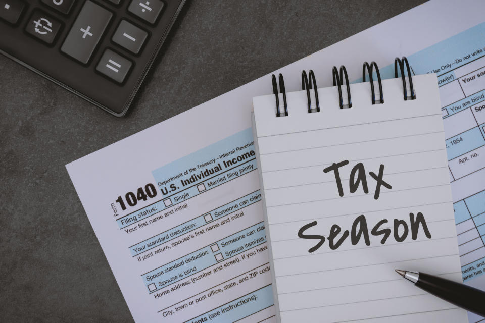 มุมมองเหนือศีรษะของ Tax Season เขียนบนแผ่นจดบันทึกและพิมพ์แบบฟอร์มภาษี