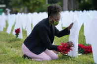 Rachel Moore writes a tribute to her cousin Wilton "Bud" Mitchell who died of COVID-19 at a symbolic cemetery created to remember and honor lives lost to COVID-19, Tuesday, Nov. 24, 2020, in the Liberty City neighborhood of Miami. Officials announced that a new COVID-19 testing site will be opening in the neighborhood. (AP Photo/Lynne Sladky)