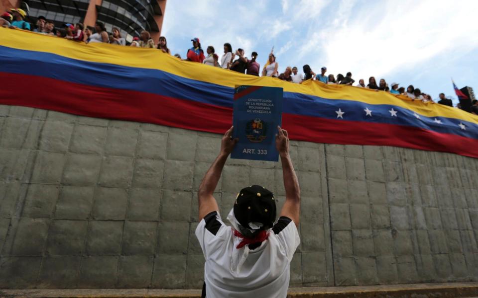 An anti-government demonstrator holds up an image of Venezuela's constitution. - Credit: AP