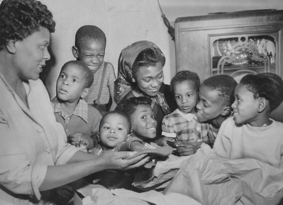 The Roy Arnold family looks over some of the Christmas gifts purchased with a $100 gift from an unknown benefactor in 1954. Pictured from left are mother Helen Arnold with children Gary, 4, John, 6, Gerald, 18 months, Gale, 7, Cathy, 13, Carla, 3, Royal, 10, and Mona, 8.