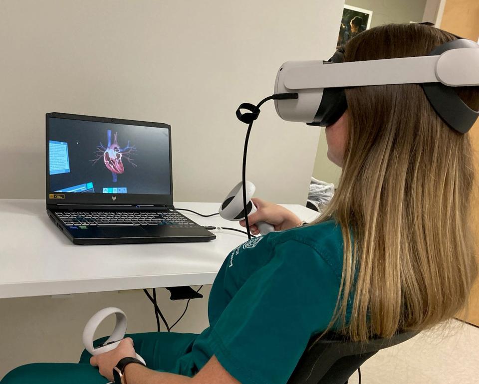A healthcare student uses virtual reality headgear and controls to examine a virtual heart inside Jacksonville University's STEAM Institute.