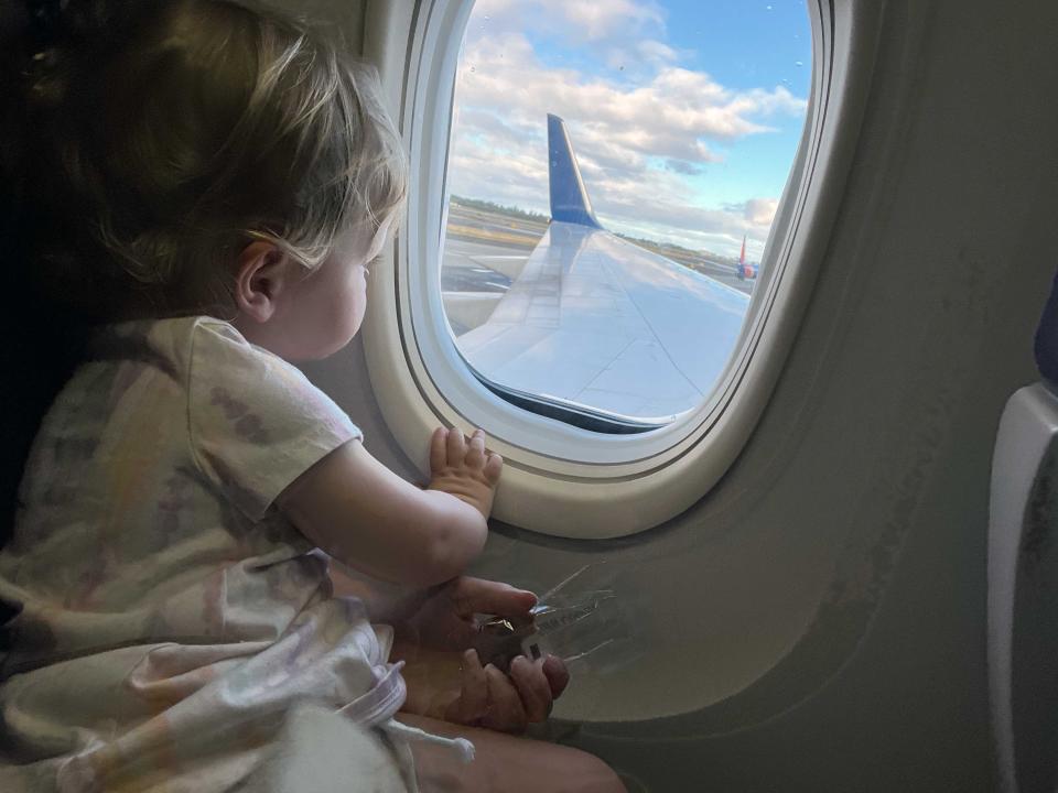 A child sitting on an airplane looking out the window with the plane's wing visible.