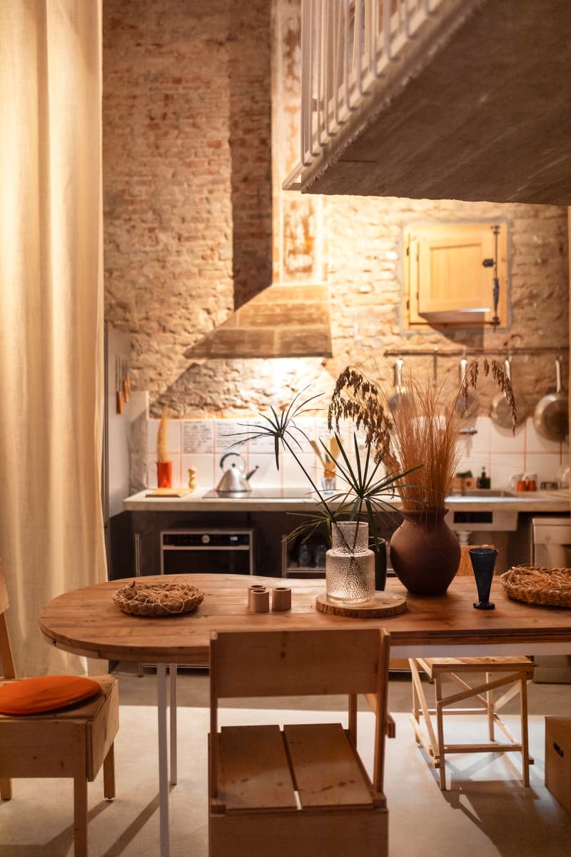 dining room with wavy wood table, exposed brick, and view of kitchen behind