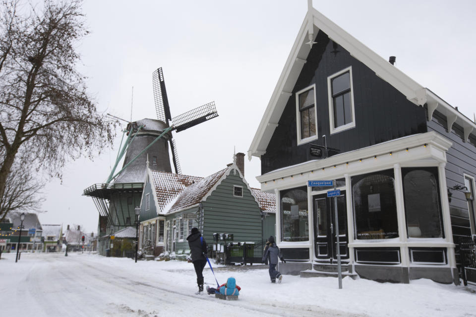 A woman pulls her child on a sled in Zaandam, near Amsterdam, Netherlands, Sunday, Feb. 7, 2021. Snow and strong winds pounded The Netherlands, with more cold and snow expected in the days ahead. (AP Photo/Peter Dejong)