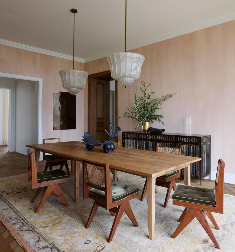 In the dining room with hand-painted and custom-tinted plaster walls, an Iranian rug from Oscar Isberian anchors an antique oak table and Pierre Jeanneret’s Chandigarh chairs. The fluted details of a glass-and-steel buffet by Christophe Côme complement similar forms in the Rose Uniacke pendant lamps.