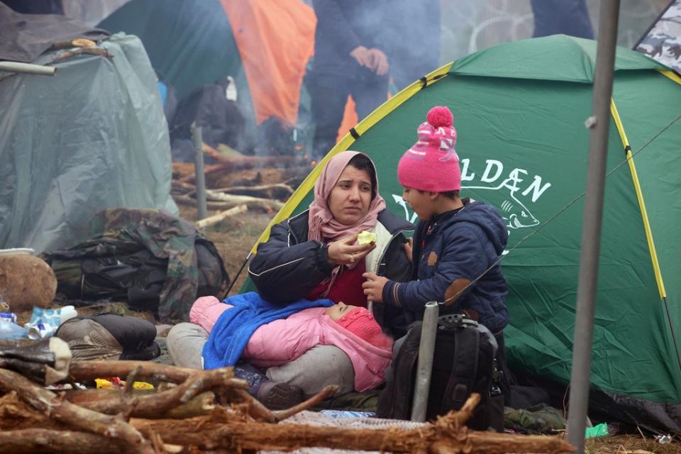 A woman and her child rest as other migrants from the Middle East and elsewhere gather at the border (AP)