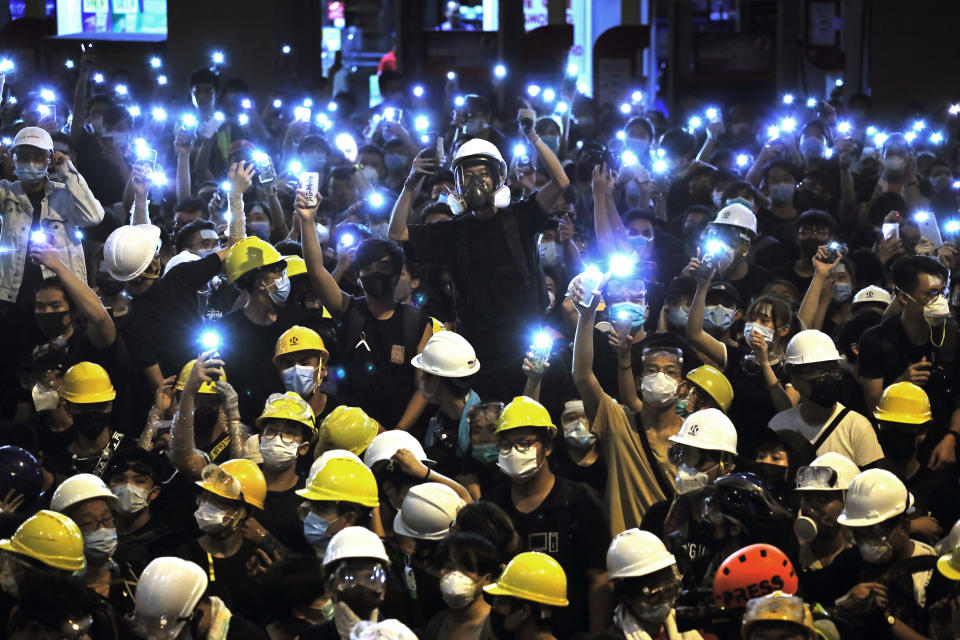 FILE - In the Friday, June 21, 2019, file photo, protesters wearing yellow hardhats hold up mobile phone lights in front of police headquarters in Hong Kong, If yellow umbrellas were the iconic accessory of the 2014 protests, yellow hardhats may be this year's. During the most violent clashes, police have used pepper spray, bean bag rounds, rubber bullets and tear gas on protesters. In response, they have donned face masks, goggles and helmets. (AP Photo/Vincent Yu, File)