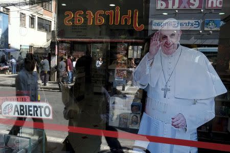 Pedestrians are reflected in a shop window which shows an image of Pope Francis in La Paz, July 1, 2015. REUTERS/David Mercado