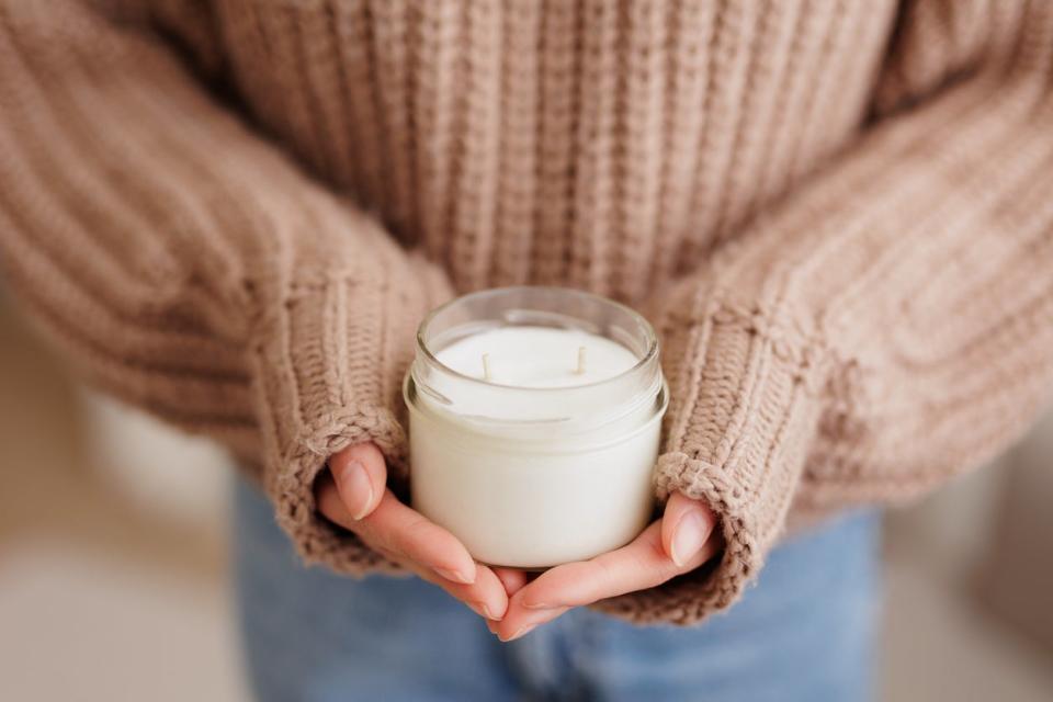 Woman in brown sweater holding an unlit white candle in her hands.