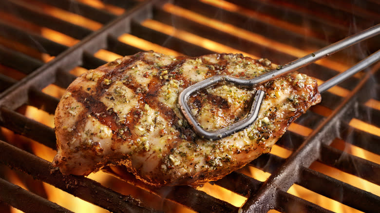 chicken breast in tongs on fiery grill