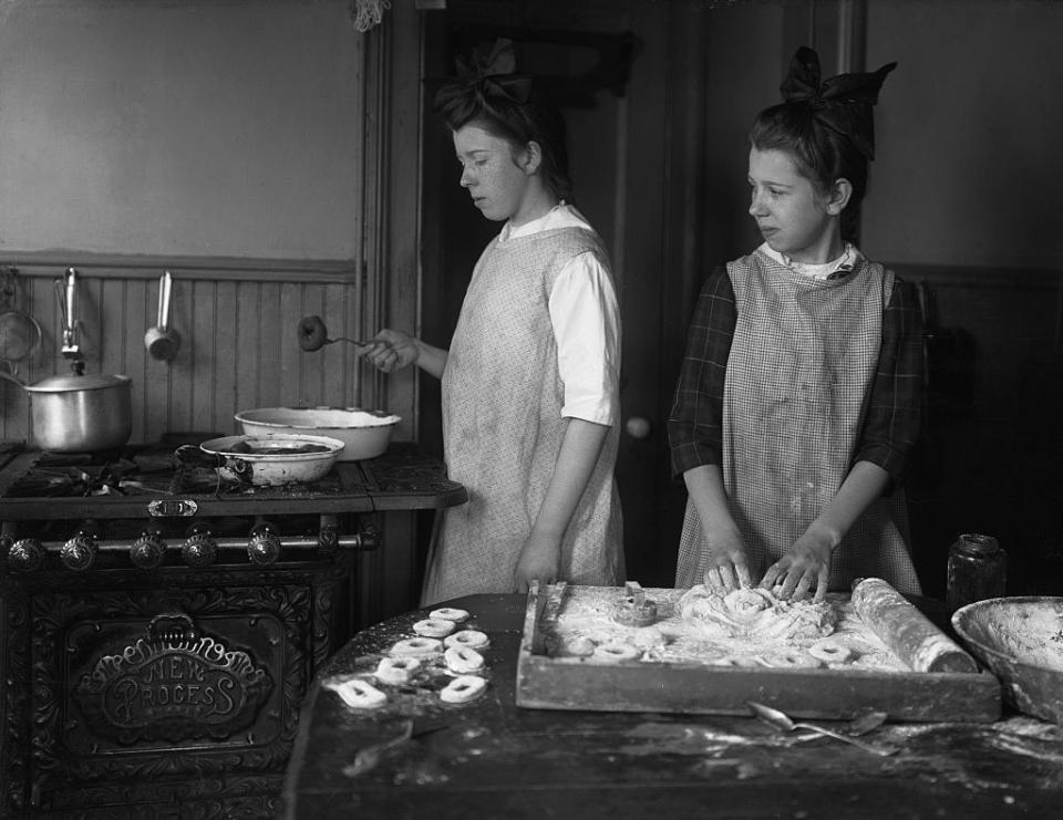 Two girls in plain smocks work side by side on the donuts