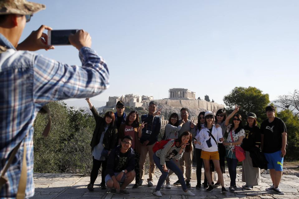 Tourists from Taiwan take photographs with the closed Acropolis ancient site in the background in Athens, Thursday, Oct. 11, 2018 during a 24-hour strike called by a Greek union representing staff at the country's ancient site. The union accused the Greek government of failing to list publicly-owned properties that have been transferred to a powerful privatization fund created during the country's international bailouts. (AP Photo/Thanassis Stavrakis)