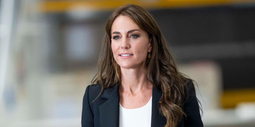 kate middleton looking away from the camera wearing a navy suit and white t shirt