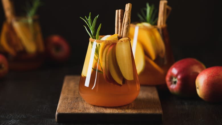 An apple cider bourbon cocktail garnished with cinnamon sticks and apples