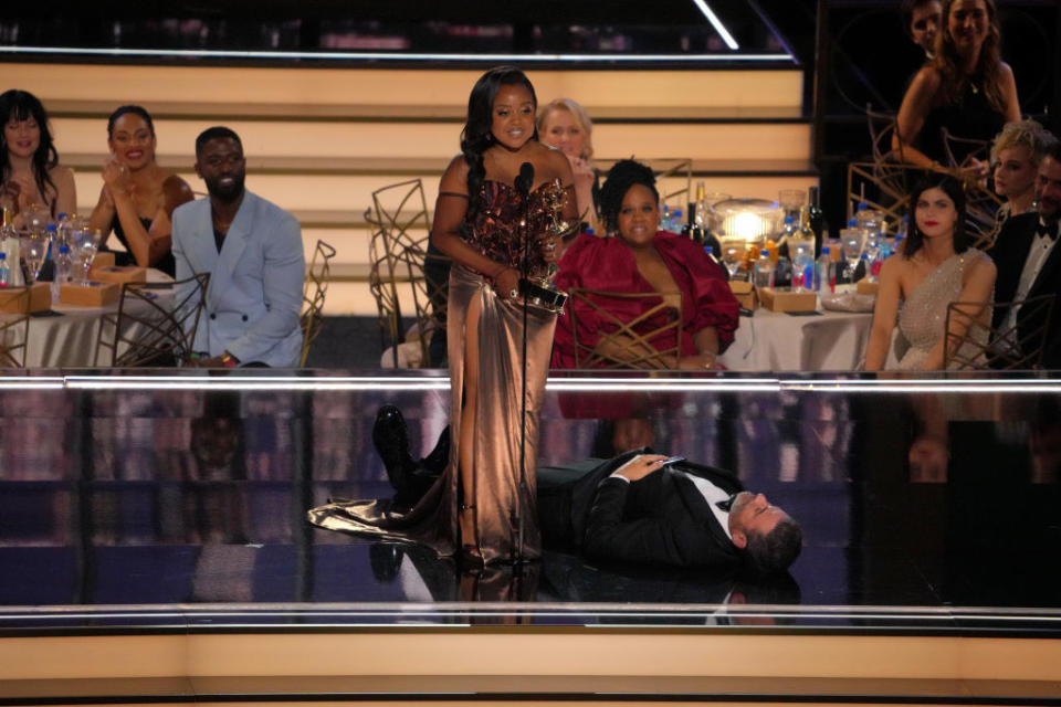 Quinta accepting her award with Jimmy lying below her