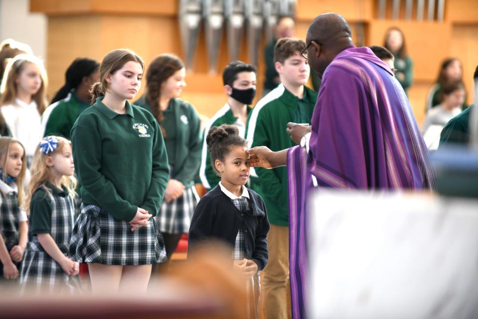 Rev. Benson Okpara applies ashes to the forehead of St. Michael the Archangel Catholic School kindergarten student Zoey Howard during  Ash Wednesday Mass at St. Michael Catholic Church in Plain Township.