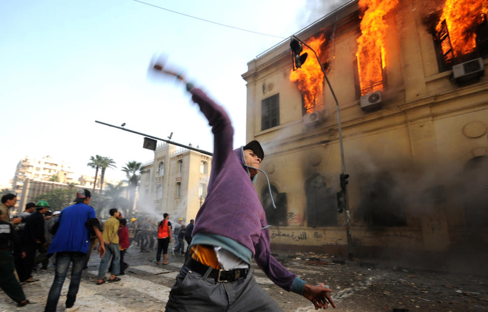 FILE - In this Dec. 17, 2011 file photo, an Egyptian protester throws a stone toward soldiers, unseen, as a building burns during clashes near Tahrir Square, in Cairo, Egypt. In an authoritative report due out Monday, March 31, 2014, a United Nations climate panel for the first time is connecting hotter global temperatures to hotter global tempers. Top scientists are saying that climate change will complicate and worsen existing global security problems, such as civil wars, strife between nations and refugees. (AP Photo/Ahmad Hammad, File)