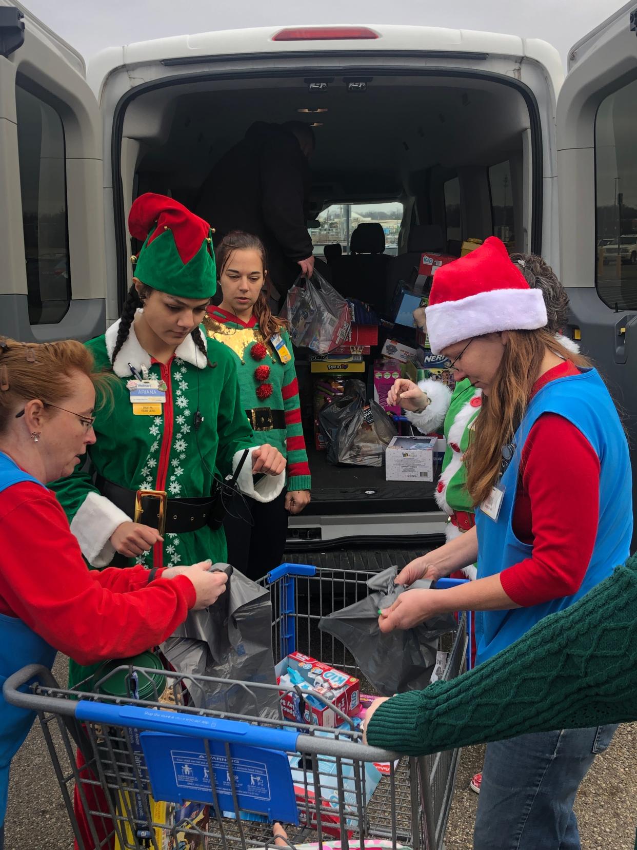 A group of Alliance Walmart employees, some in elf costumes, load donated toys into a van for the Alliance chapter of the Salvation Army.