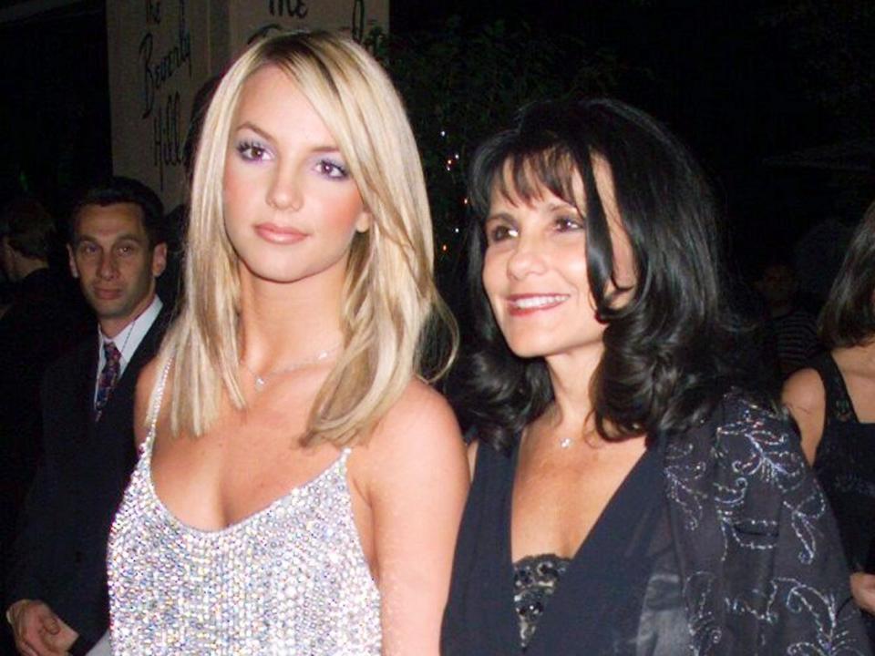 Britney Spears (tall, blonde, wearing a sequined tank top and light pink pants) standing next to her mother Lynne (shorter, dark-haired woman in black floor-length gown).