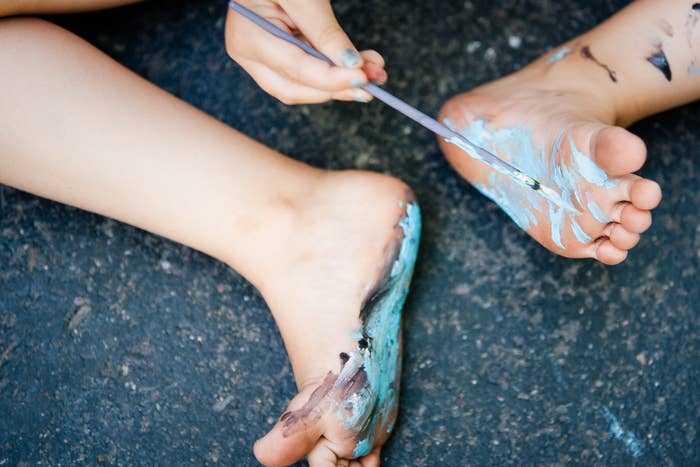 Child painting their feet with a brush and blue paint